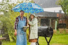 Dva lidé stojí na zahradě u grilu v dešti pod deštníkem