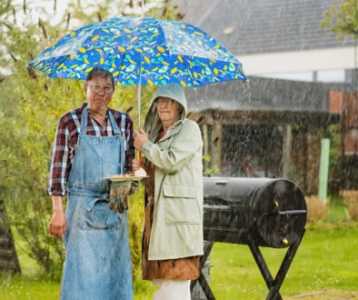 Dva lidé stojí na zahradě u grilu v dešti pod deštníkem