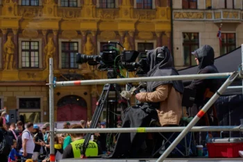 muž pod plachtou stojící na lešení s kamerou