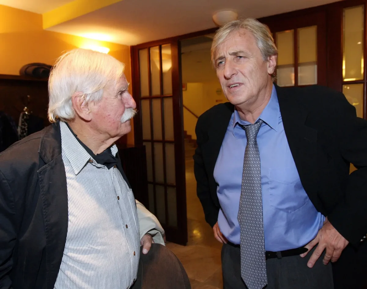 Šlo o poslední televizní roli herce Karla Heřmánka. Zdroj: Profimedia | TVGURU.cz Two older men in business attire converse in a hallway, one holding a coat over his arm.