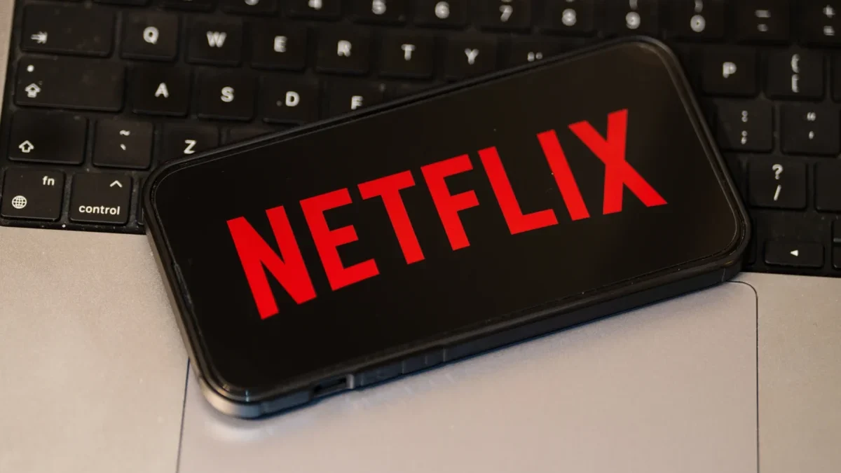 Na notebooku leží mobil s logem Netflixu.