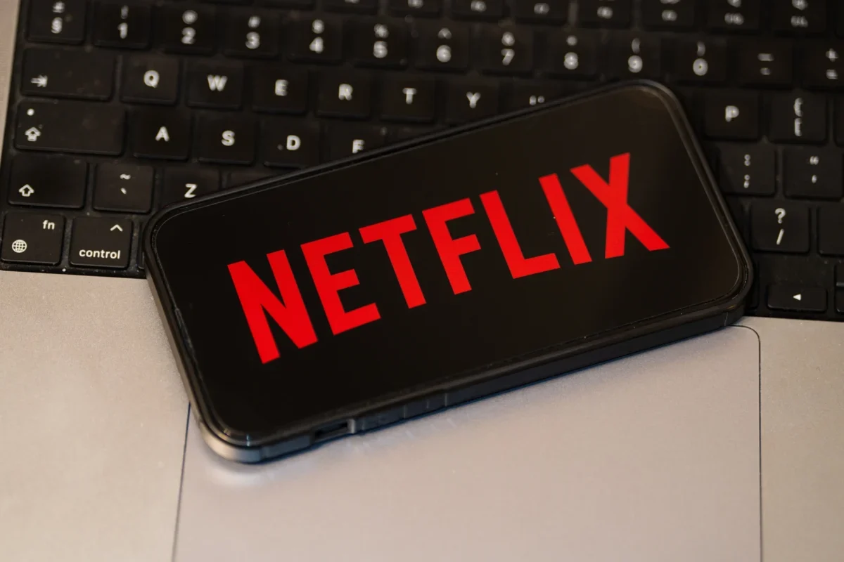 Na notebooku leží mobil s logem Netflixu.
