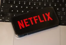 Na notebooku leží mobil s logem Netflixu.