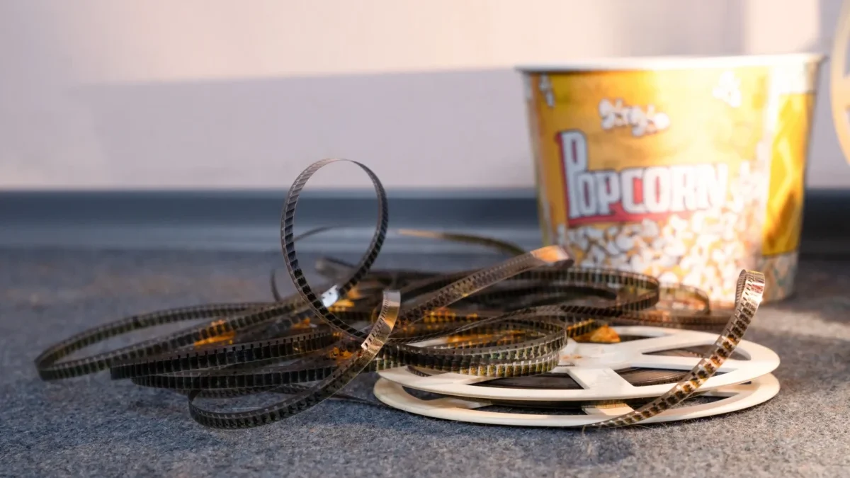 Coiled strips of movie film spread across a carpet with a yellow popcorn bucket in the background.