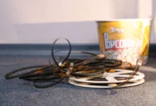 Coiled strips of movie film spread across a carpet with a yellow popcorn bucket in the background.