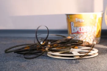 Coiled strips of movie film spread across a carpet with a yellow popcorn bucket in the background.