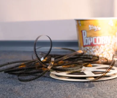 Coiled strips of movie film spread across a carpet with a yellow popcorn bucket in the background.
