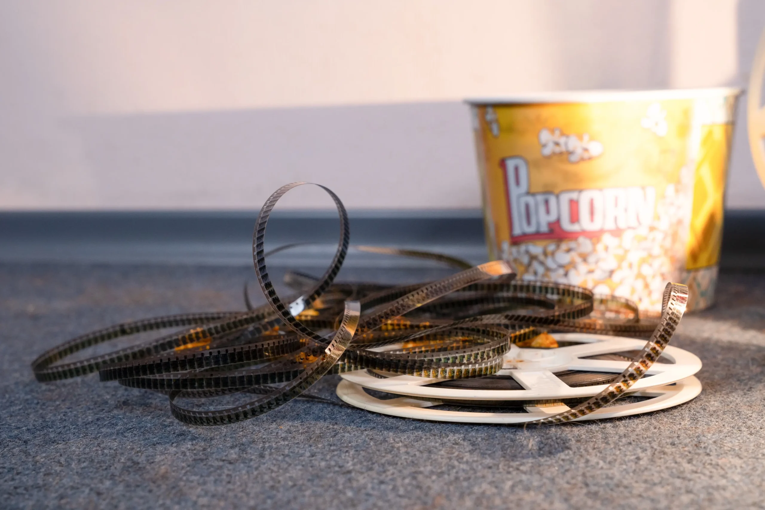 Coiled strips of movie film spread across a carpet with a yellow popcorn bucket in the background.