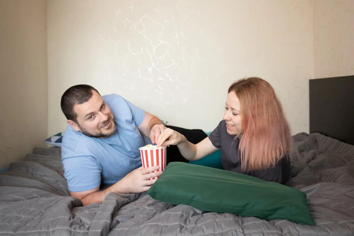 shutterstock_2526922085-2 | TVGURU.cz Žena s mužem leží společně s popcornem na posteli.