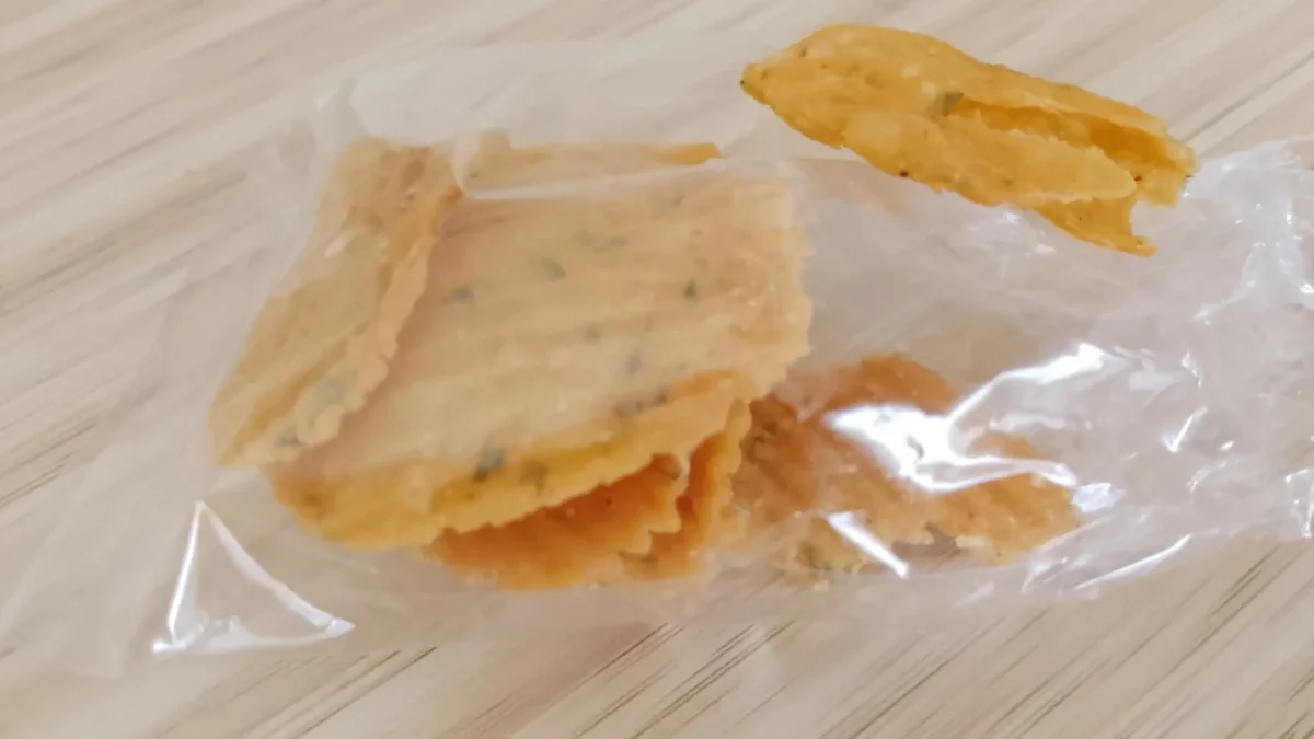 Golden fried snack piece resting on a clear plastic bag on a light wooden surface