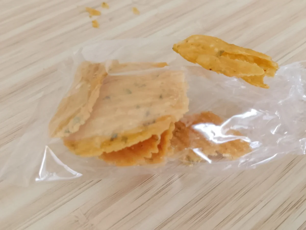 Golden fried snack piece resting on a clear plastic bag on a light wooden surface