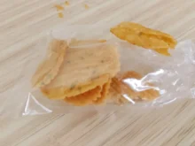 Golden fried snack piece resting on a clear plastic bag on a light wooden surface
