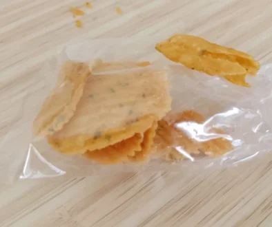Golden fried snack piece resting on a clear plastic bag on a light wooden surface