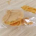 Golden fried snack piece resting on a clear plastic bag on a light wooden surface