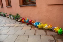 Row of colorful plastic children's watering cans and small planters lined up along a peach wall.