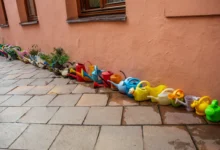 Row of colorful plastic children's watering cans and small planters lined up along a peach wall.