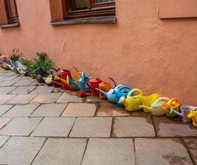 Row of colorful plastic children's watering cans and small planters lined up along a peach wall.
