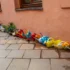 Row of colorful plastic children's watering cans and small planters lined up along a peach wall.