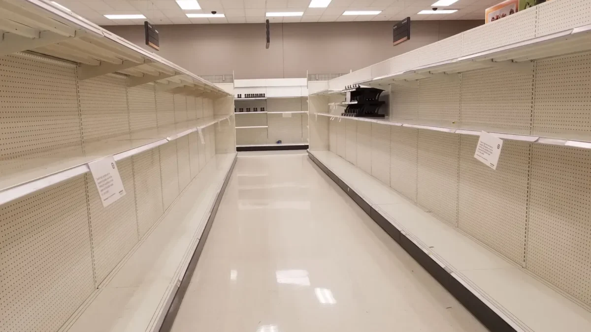Empty supermarket aisle with bare shelves on both sides and bright ceiling lights.