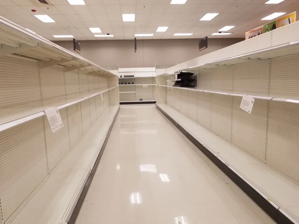 Empty supermarket aisle with bare shelves on both sides and bright ceiling lights.
