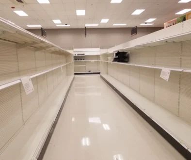 Empty supermarket aisle with bare shelves on both sides and bright ceiling lights.
