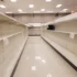 Empty supermarket aisle with bare shelves on both sides and bright ceiling lights.