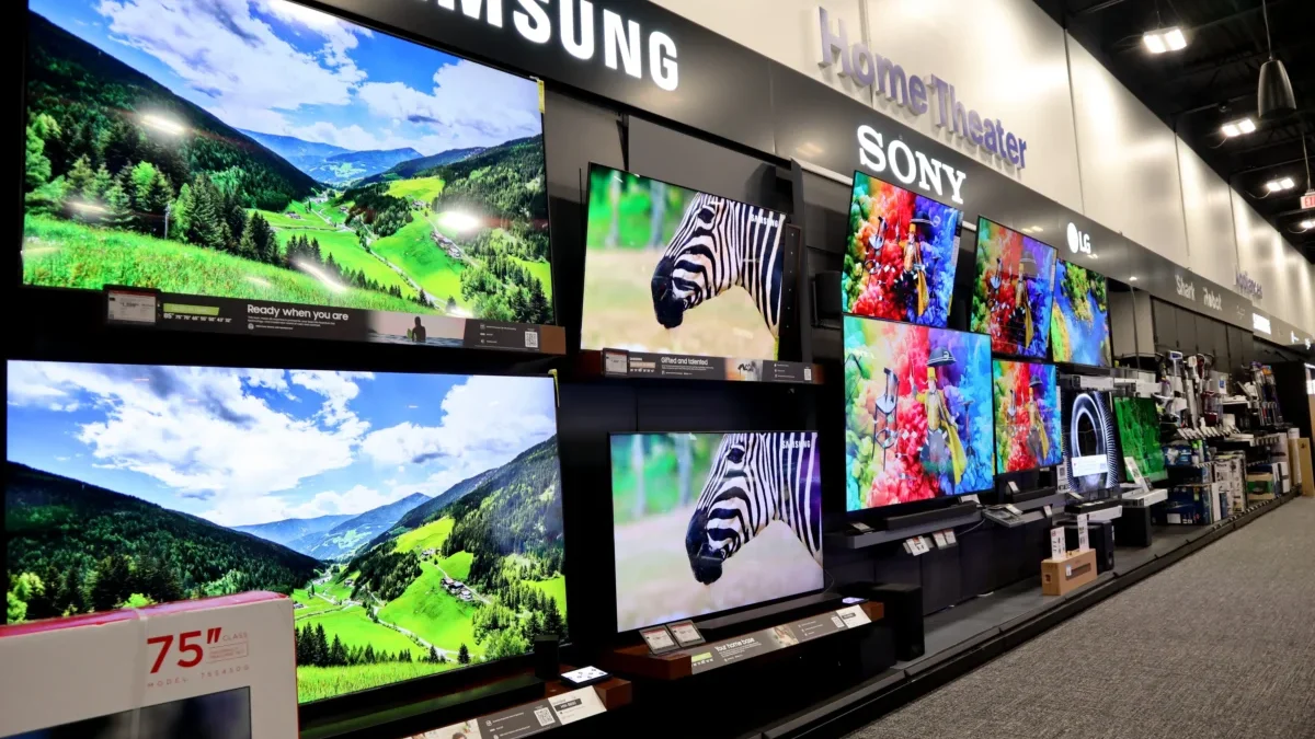 Showroom wall with large flat-screen TVs displaying colorful landscapes and product brands like Samsung, Sony, and LG
