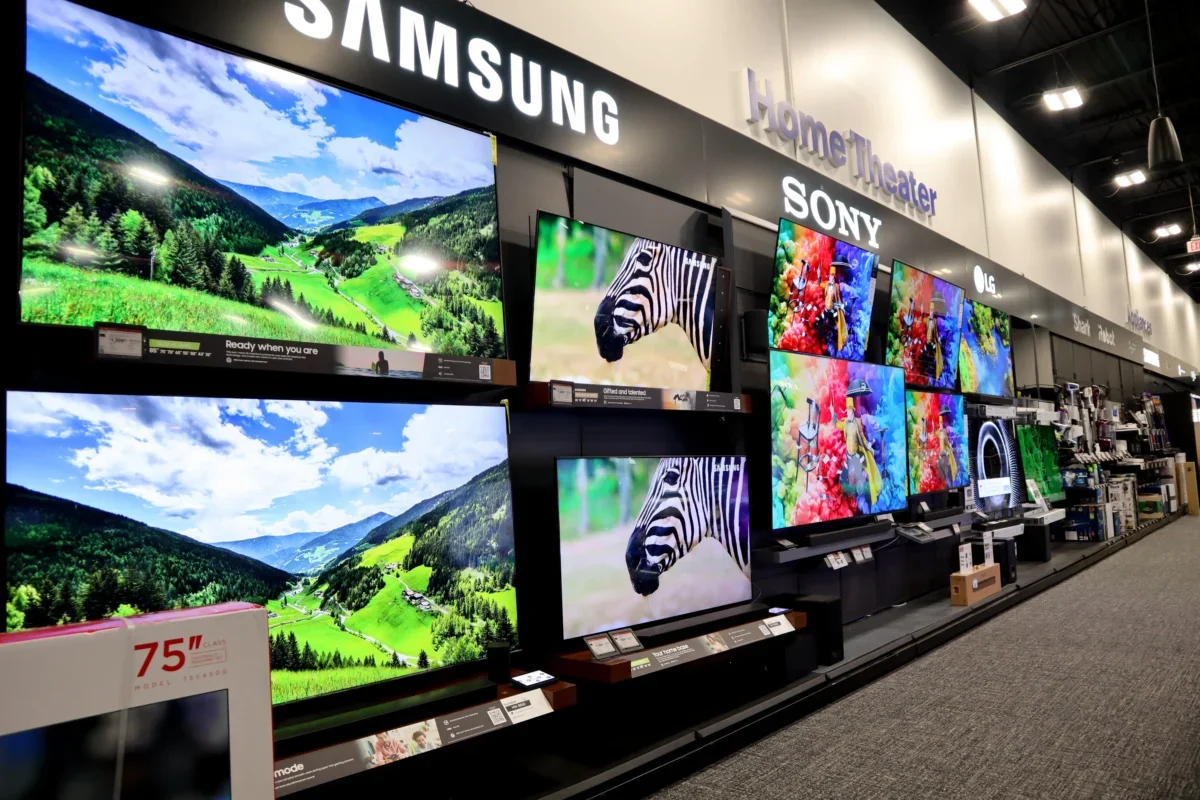 Showroom wall with large flat-screen TVs displaying colorful landscapes and product brands like Samsung, Sony, and LG