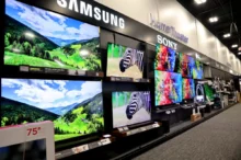 Showroom wall with large flat-screen TVs displaying colorful landscapes and product brands like Samsung, Sony, and LG