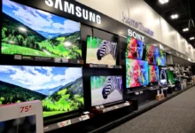Showroom wall with large flat-screen TVs displaying colorful landscapes and product brands like Samsung, Sony, and LG