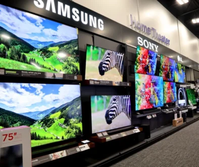 Showroom wall with large flat-screen TVs displaying colorful landscapes and product brands like Samsung, Sony, and LG