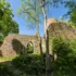 Old stone ruin with arched doorway, surrounded by dense greenery and trees under a bright blue sky