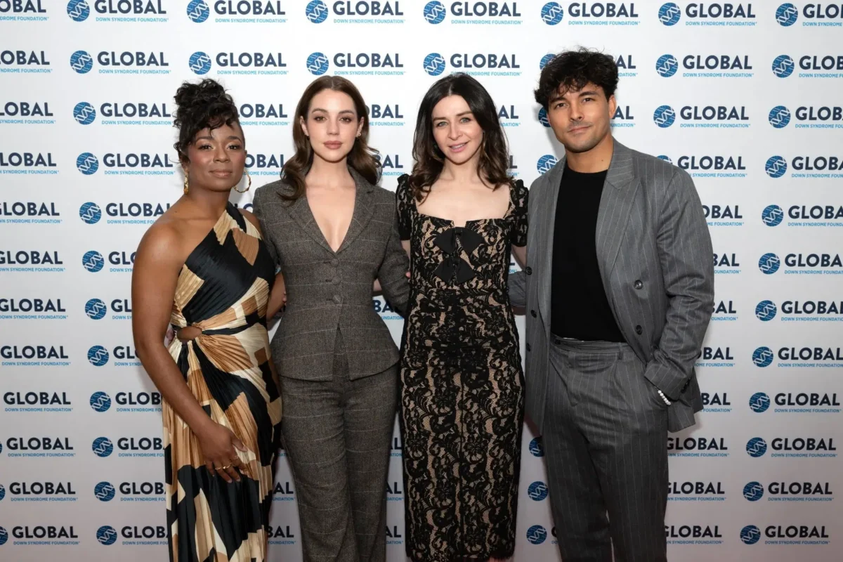profimedia-0935361584 1 | TVGURU.cz Four adults pose in front of a Global Down Syndrome Foundation backdrop; from left: woman in a color-block dress, woman in a gray plaid suit, woman in a black lace dress, man in a gray pinstripe suit.