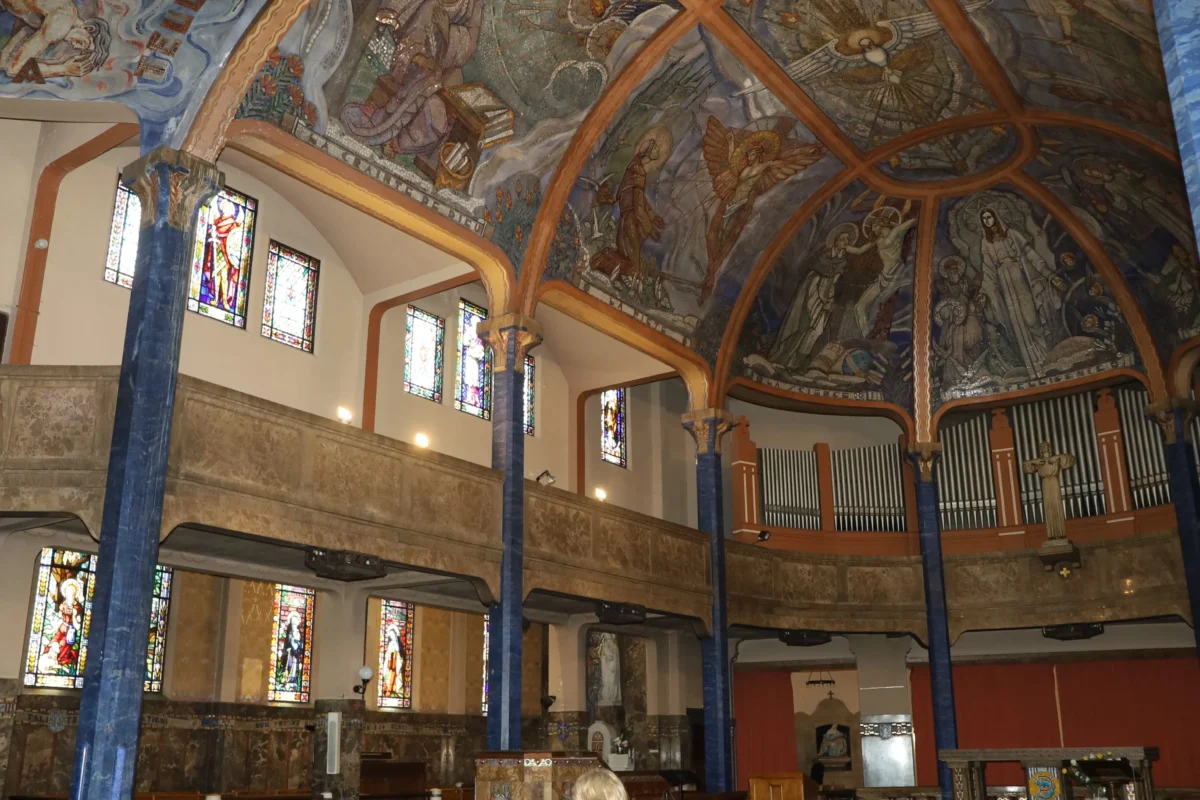 shutterstock_2148621917 1 | TVGURU.cz Interior of a church with blue marble pillars, colorful ceiling murals, and stained-glass windows along the walls