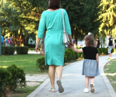 Žena jde s holčičkou za ruku po chodníku.