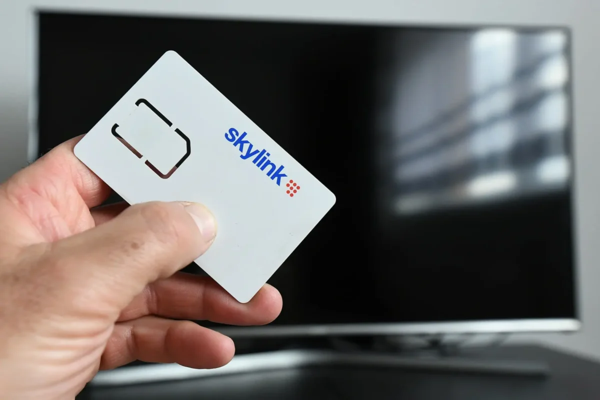 profimedia-0668491909 1 | TVGURU.cz Close-up of a hand holding a SkyLink card in front of a turned-off monitor or TV screen.