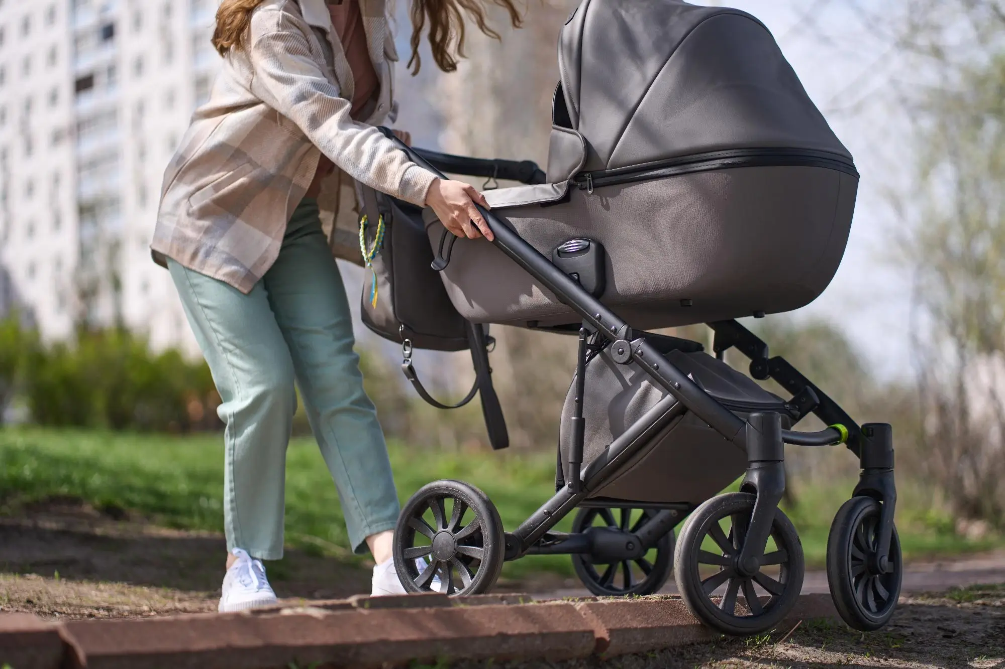 Person pushing a gray baby stroller attached to a bicycle on a park path outdoor scene