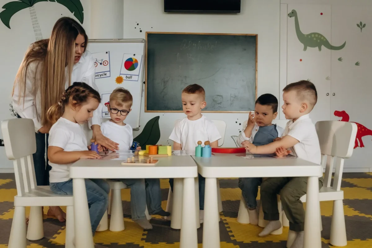 Děti ve školce u stolu a stojící učitelka