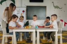 Děti ve školce u stolu a stojící učitelka