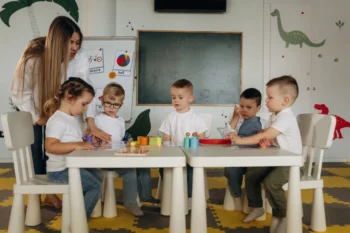 Děti ve školce u stolu a stojící učitelka