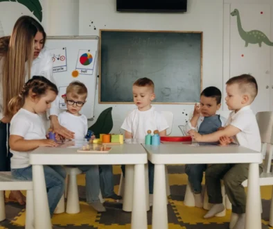 Děti ve školce u stolu a stojící učitelka