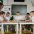 Děti ve školce u stolu a stojící učitelka