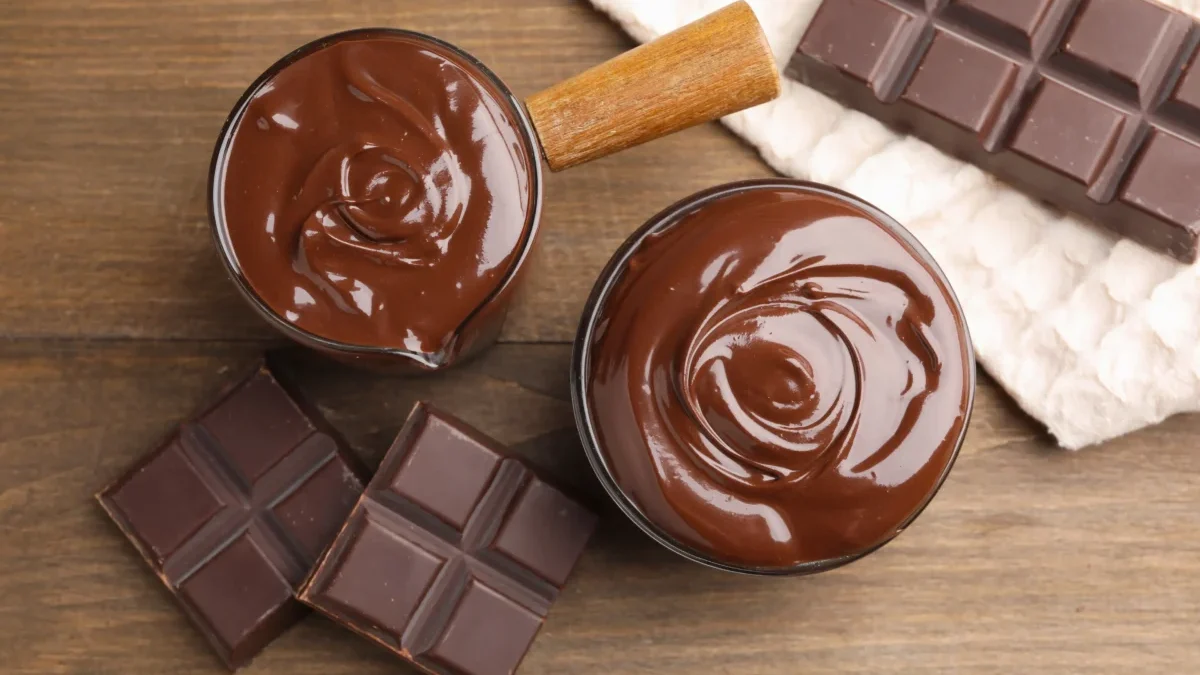 Top-down view of melted chocolate in two bowls with broken chocolate bars on a wooden surface.