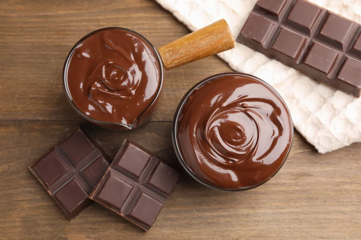 Top-down view of melted chocolate in two bowls with broken chocolate bars on a wooden surface.