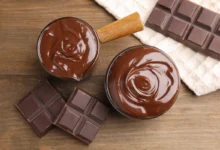 Top-down view of melted chocolate in two bowls with broken chocolate bars on a wooden surface.