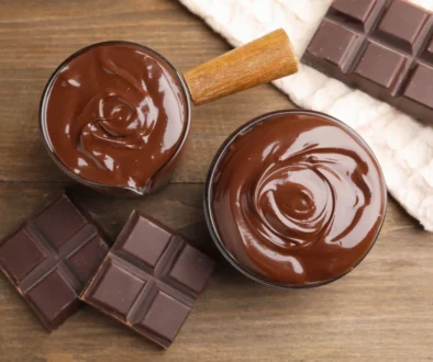 Top-down view of melted chocolate in two bowls with broken chocolate bars on a wooden surface.