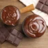 Top-down view of melted chocolate in two bowls with broken chocolate bars on a wooden surface.