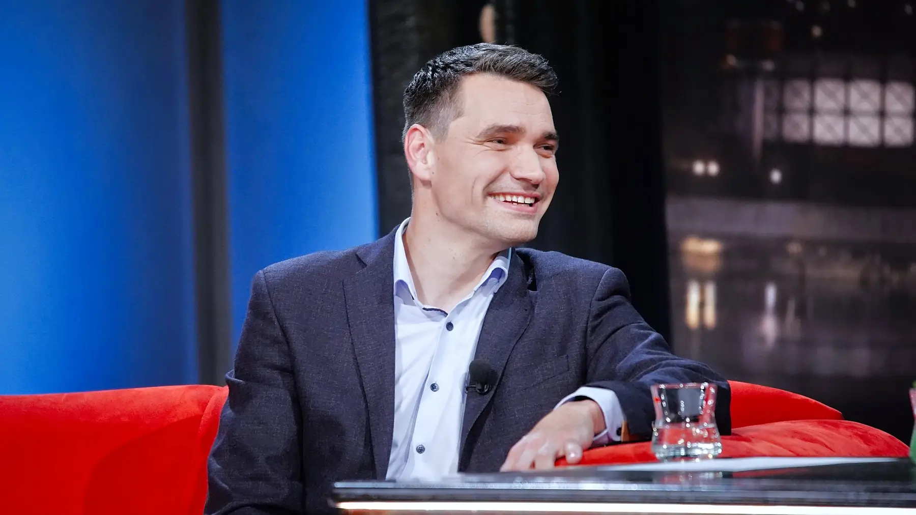 Moderátor Daniel Stach sedí na gauči.