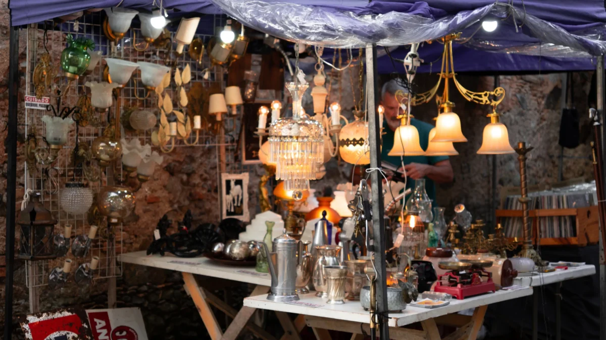 Market stall selling vintage lighting: brass lamps, crystal chandeliers, and glass lamps under a purple canopy.