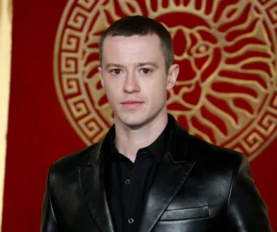 Joseph Quinn stojí u červené zdi.
